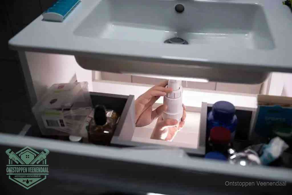 Een pompfles met zeep boven een wastafel, de heet water en afwasmiddel-methode om een vetprop in de afvoer los te maken in Veenendaal