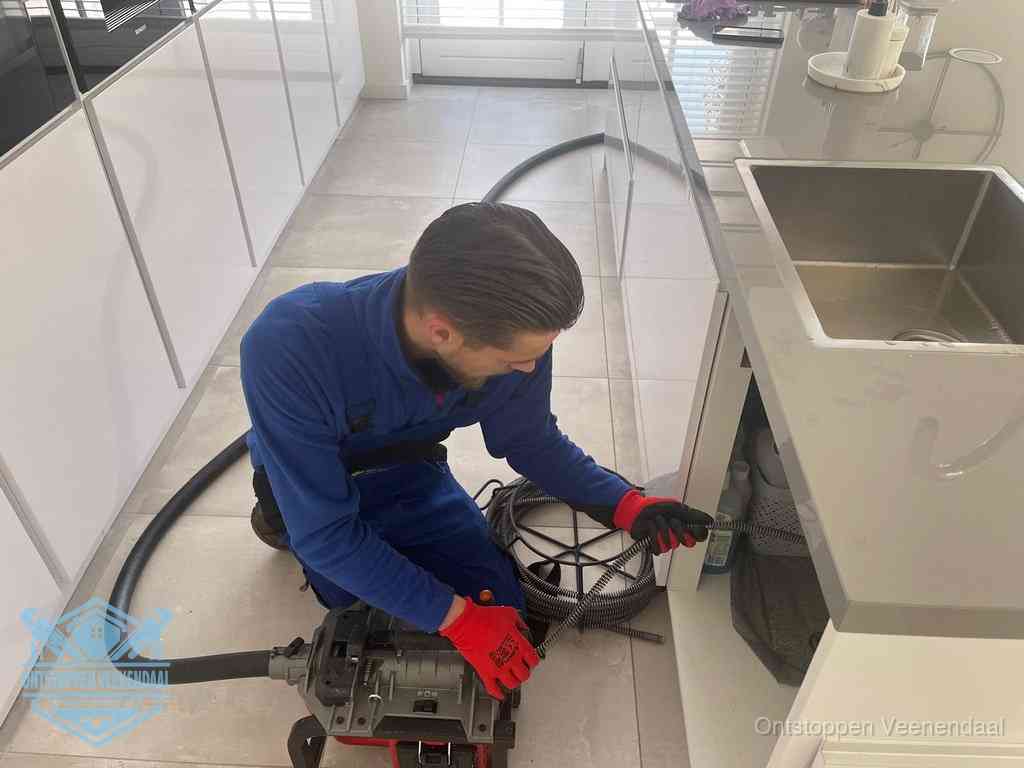 Een monteur ontstopt de keukenafvoer onder de spoelbak met een elektrische veermachine in Veenendaal