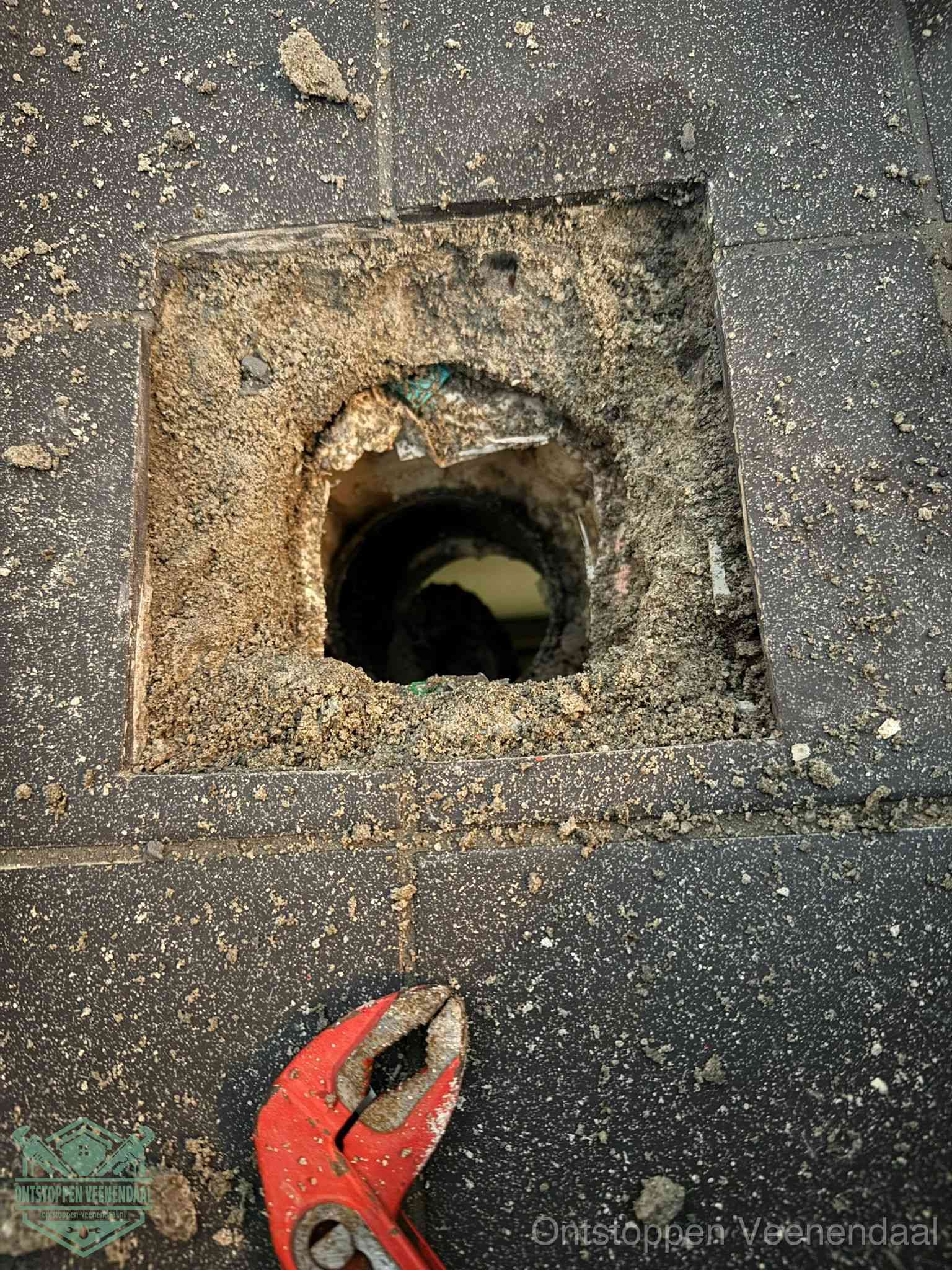 Een geopend rioolputje in een betontegelvloer met losgemaakt rooster en een zichtbare ronde afvoerbuis, het achterhalen waar de afvoerverstopping zit in Veenendaal