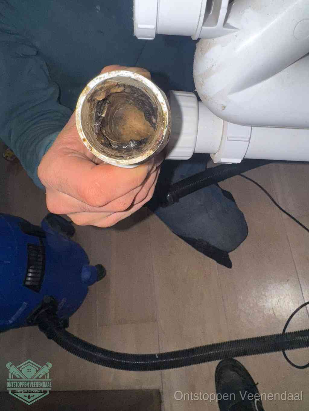 Een hand houdt een losgekoppeld PVC-afvoerbuisstuk vast dat van binnen volledig is dichtgeslibd met vet, vuil en aanslag, de meest voorkomende oorzaak van een verstopte afvoer in Veenendaal