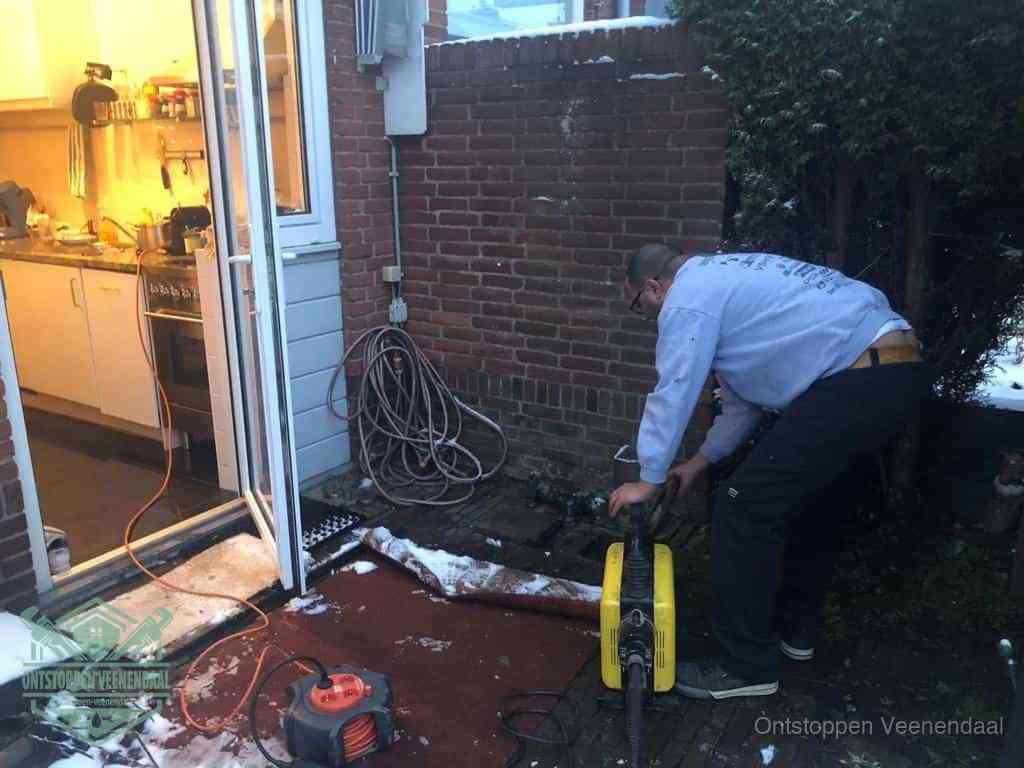 Een monteur werkt buiten bij een open riool-/grondput met een elektrische ontstoppingsmachine om een verborgen afvoerprobleem op te sporen in Veenendaal