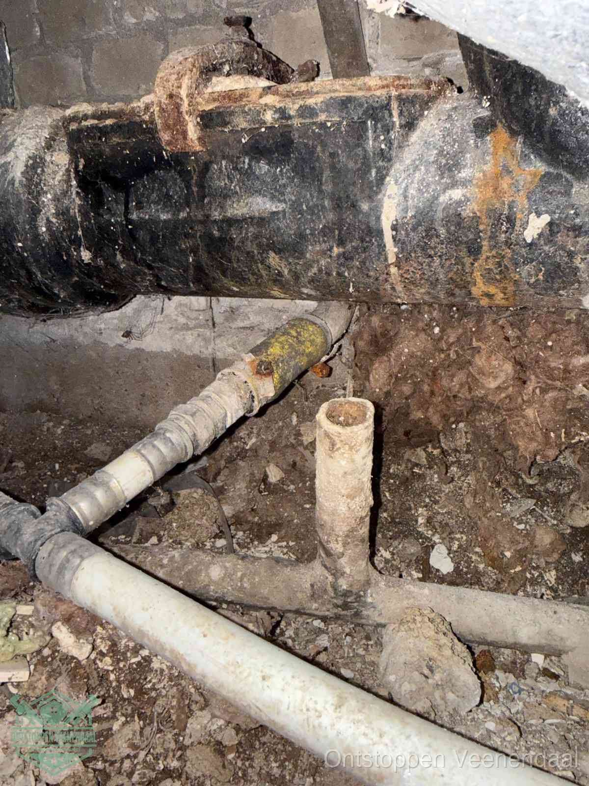 Een dikke zwarte hoofdrioolbuis met roest- en kalkaanslag in een kruipruimte, oorzaak van terugkerende structurele afvoerproblemen in Veenendaal