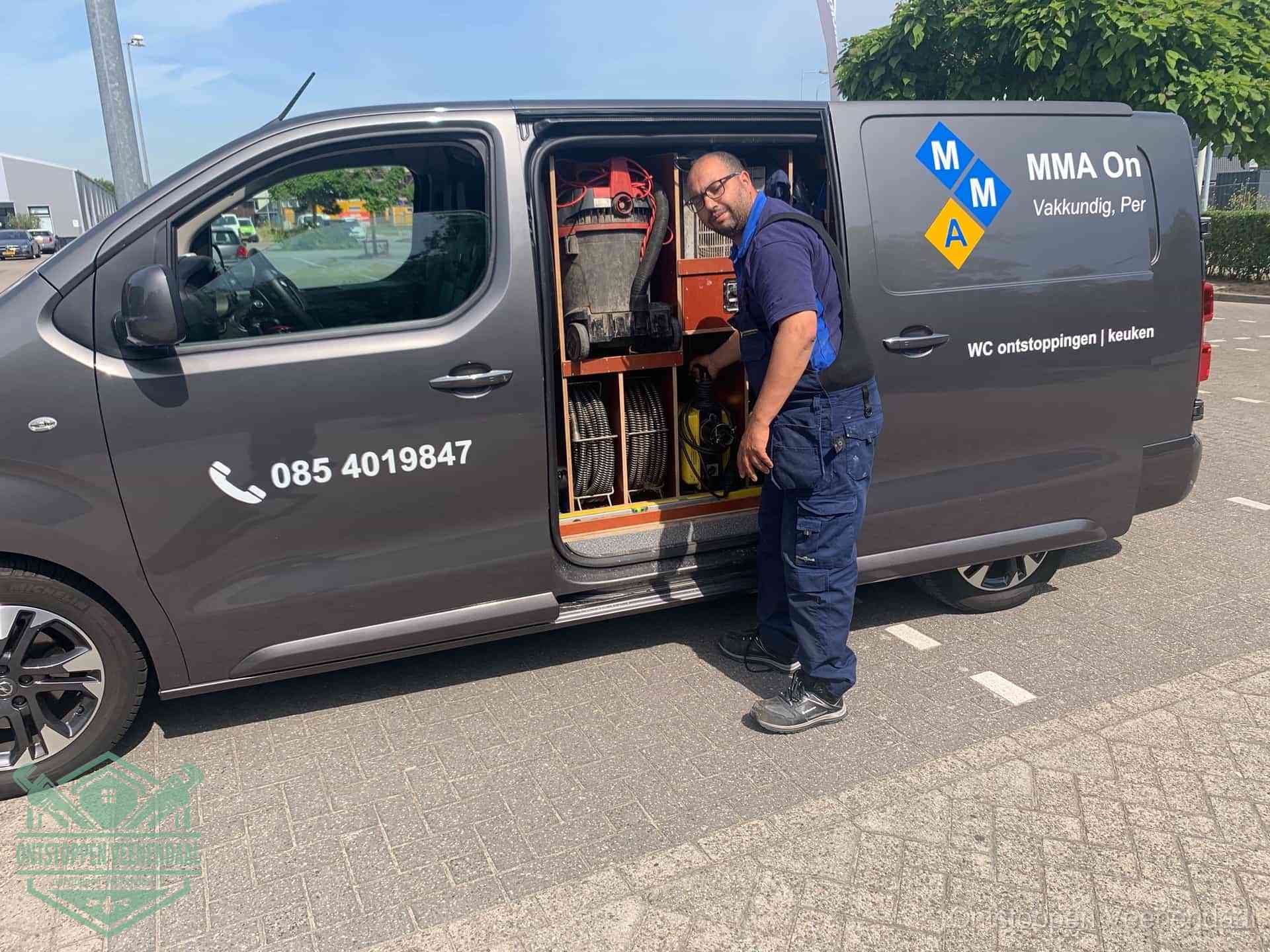 Een monteur bij de open schuifdeur van zijn bedrijfsbus op een parkeerplaats, klaar om de oorzaak van terugkerende afvoerverstoppingen aan te pakken in Veenendaal
