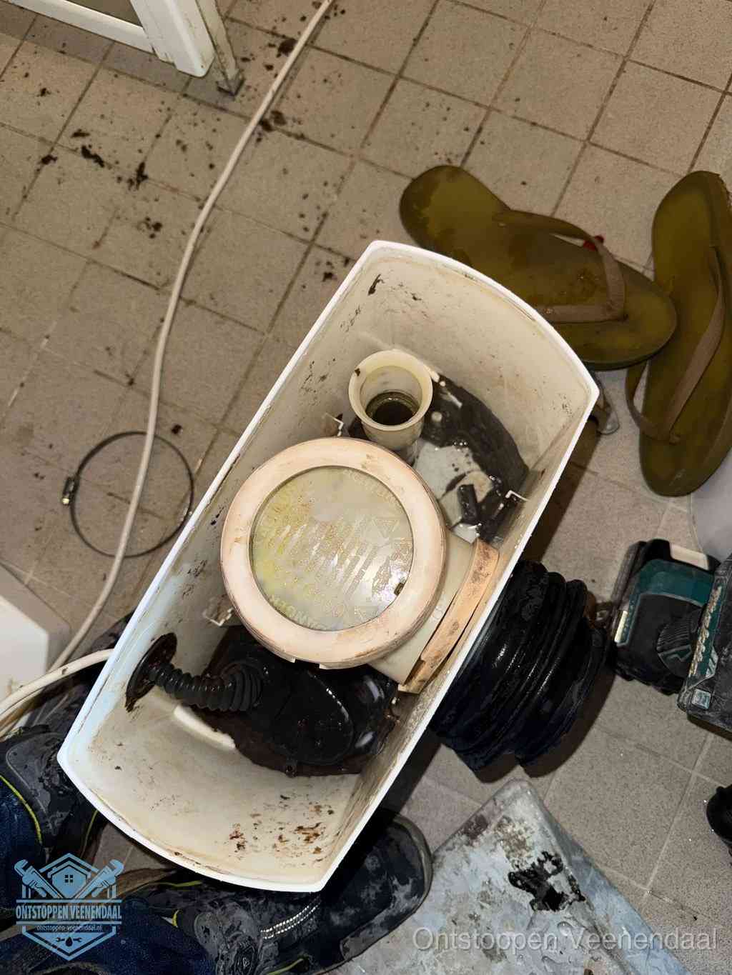 Een gedemonteerde toiletpot op de vloer met ontstoppingsveer en gereedschap ernaast, het verwijderen van een vastzittend voorwerp uit de wc in Veenendaal