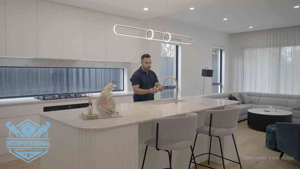 Een bewoner bij de keukenspoelbak die zelf aan de slag gaat met een verstopte gootsteen in Veenendaal